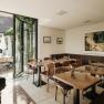 Gastzimmer wird durch Vinothek & Weinkeller ergänzt, © Niederösterreich Werbung/Michael Reidinger Gemütliches Gastzimmer mit Holztischen, Kunst an der Wand und Terrasse im Freien.