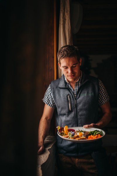 Im Service: Wirt Matthias Distelberger, © Niederösterreich Werbung/Daniela Führer Ein Mann in Tracht hält einen Teller mit Essen in der Hand.