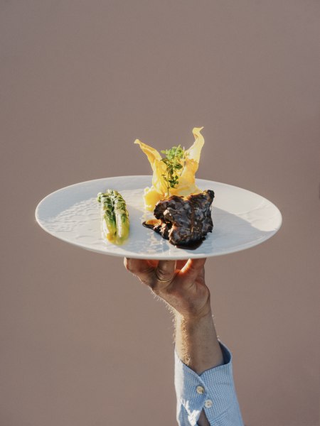 Angus Rind und Spargel, © Niederösterreich Werbung/Julius Hirtzberger Ein Teller mit Angus-Rind, Spargel und dekorativer Beilage wird von einer Hand hochgehalten.