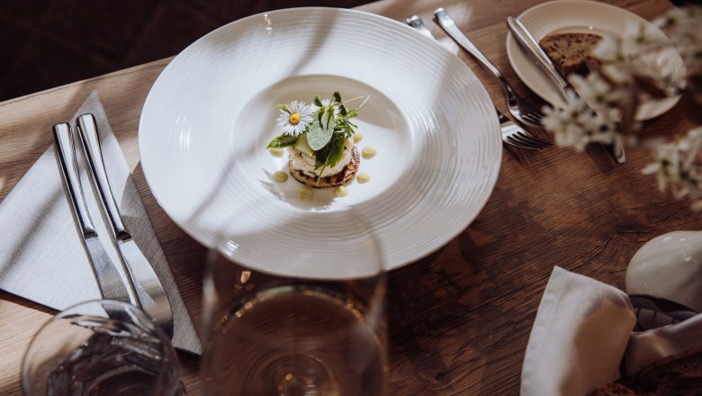 Tartar von der Räucherforelle auf Erdäpfelpuffer, © Niederösterreich Werbung/thecreatingclick.com Ein Teller mit Tartar von Räucherforelle auf einem Erdäpfelpuffer, garniert mit Kräutern und Blüten, auf einem Holztisch mit Besteck und einem Glas Wein.