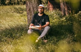 Wirt Rafael Gründlinger-Pils, © Niederösterreich Werbung/Daniela Führer Mann sitzt im Gras unter einem Baum und hält einen Teller mit Essen.