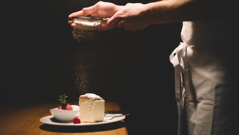 Ein Teller mit Cremeschnitte und Himbeersorbet, dar&uuml;ber wird Puderzucker gestreut.