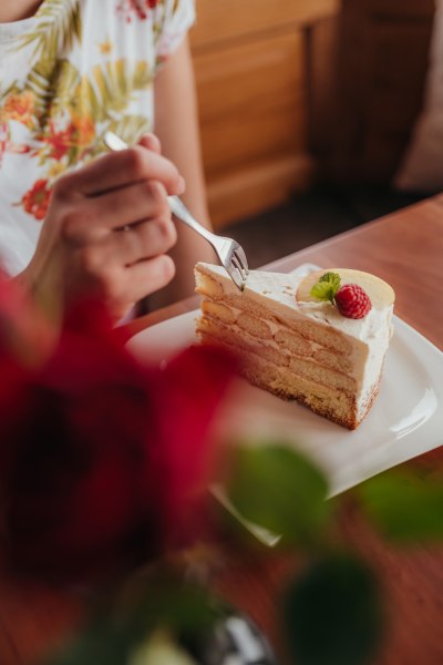 Eine Person isst ein Stück Sahnetorte mit einer Himbeere und Minzblatt auf einem Teller.