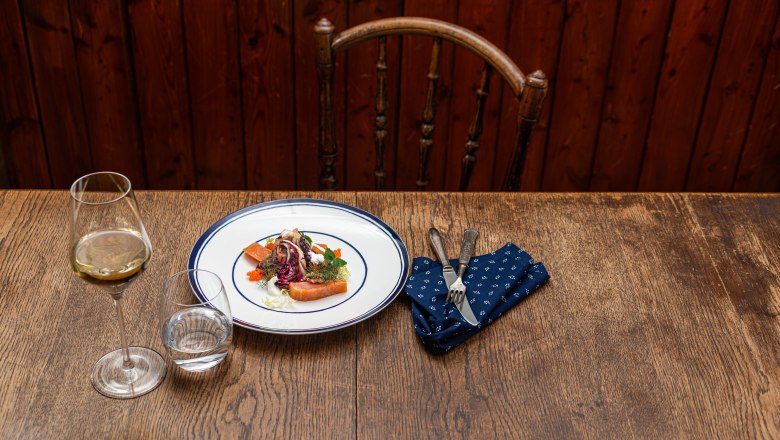 Weißer Teller mit Bratapfel und Lachsforelle auf Holztisch.