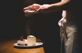 Ein Teller mit Cremeschnitte und Himbeersorbet, dar&uuml;ber wird Puderzucker gestreut.