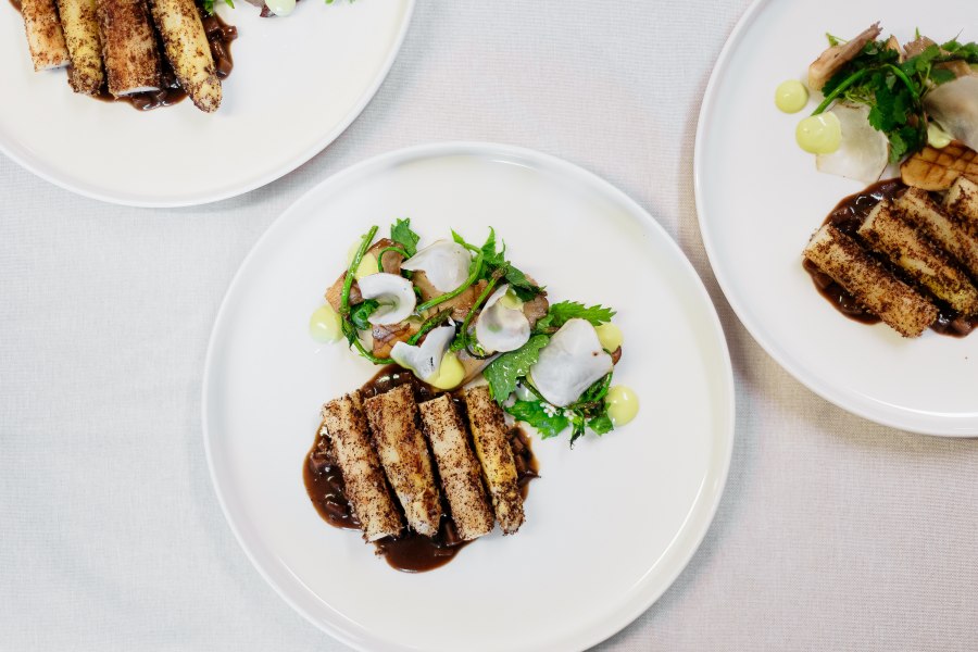 Drei Teller mit kunstvoll angerichteten Gourmetgerichten auf weißem Tischtuch.