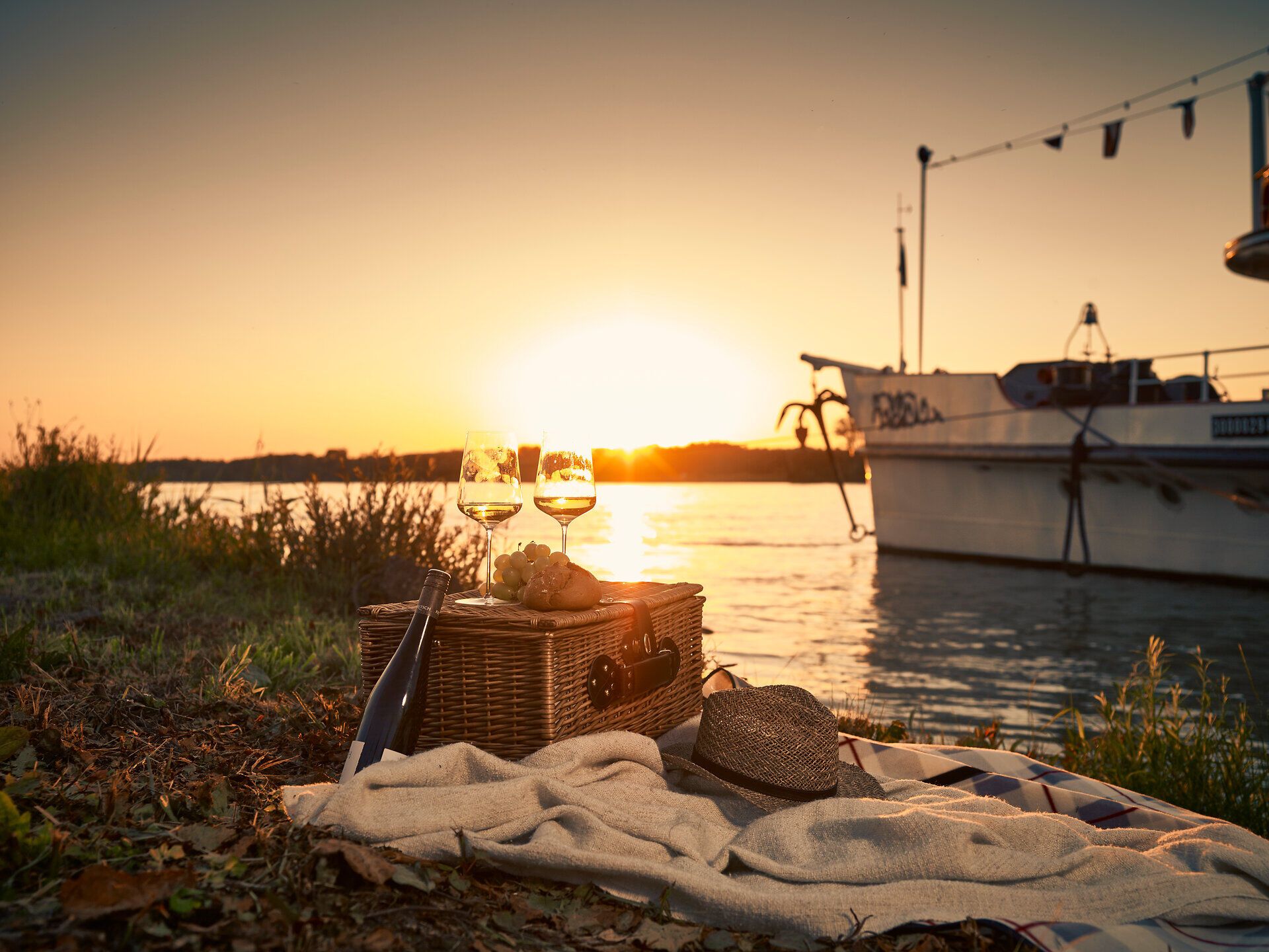 Ein romantisches Picknick am Ufer der Donau lädt dazu ein, den Sonnenuntergang in vollen Zügen zu genießen. Die Gläser mit erfrischendem Wein funkeln im warmen Licht, während die sanften Wellen des Flusses eine beruhigende Melodie spielen. Umgeben von der Schönheit der Natur und dem Duft blühender Pflanzen wird dieser Moment unvergesslich.