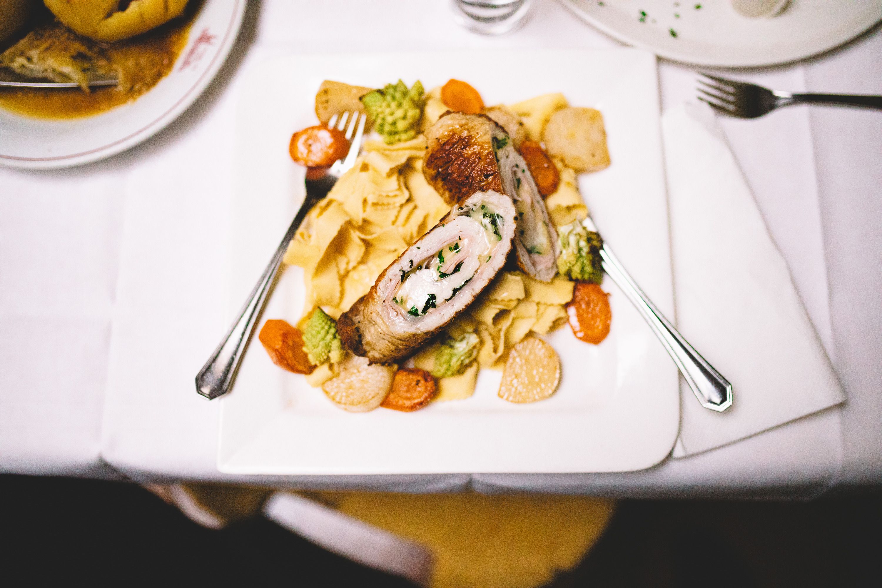 Gefülltes Fleisch auf Nudeln mit Gemüse auf einem weißen Teller.