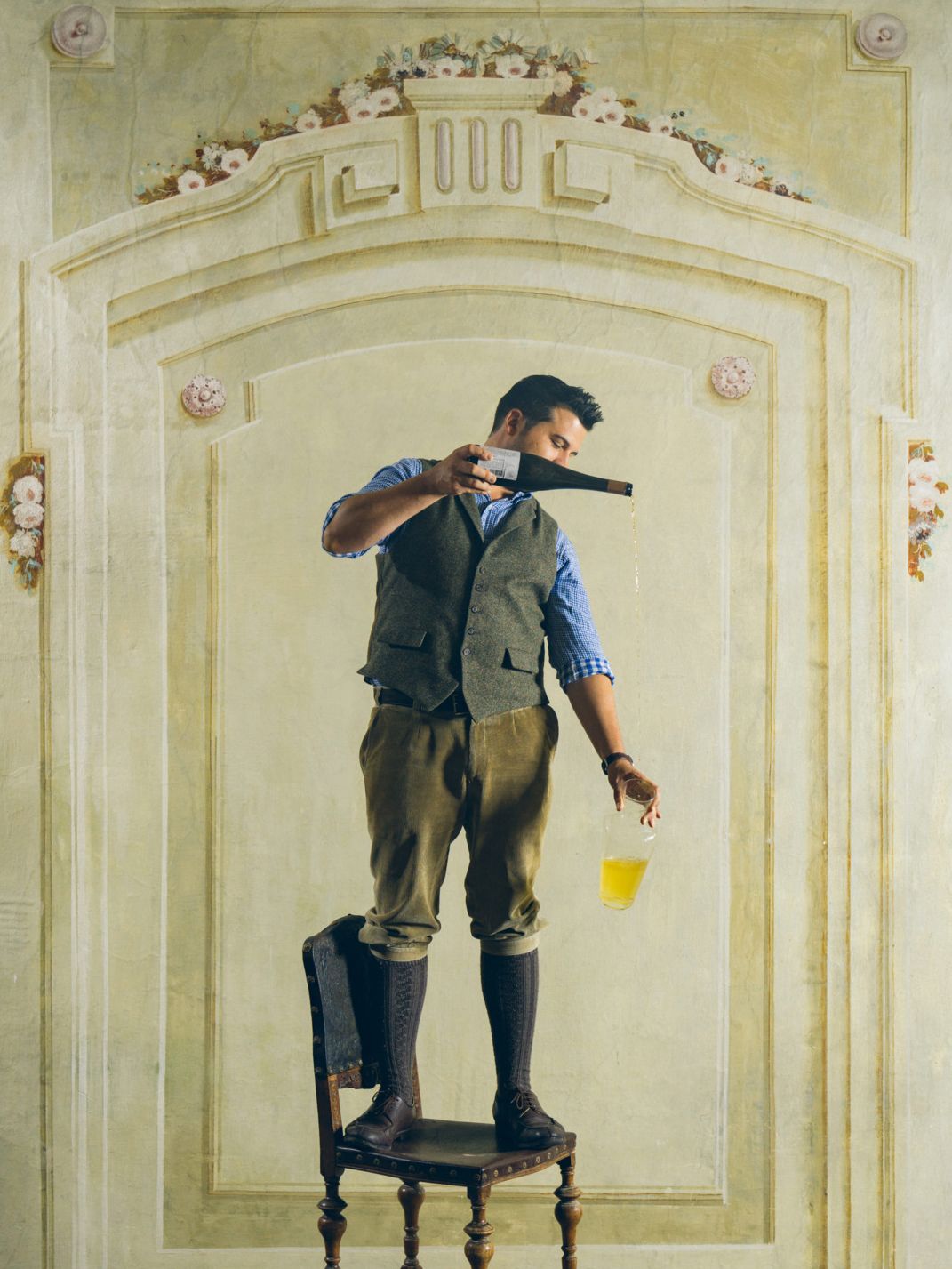 Hartmuth Rameder steht auf einem Stuhl und gießt Wein  aus einer Flasche in ein Glas.