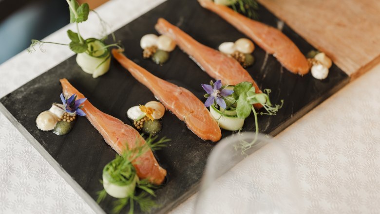 Gourmetgericht mit Lachs, Kr&auml;utern und Bl&uuml;ten auf Schieferplatte serviert.