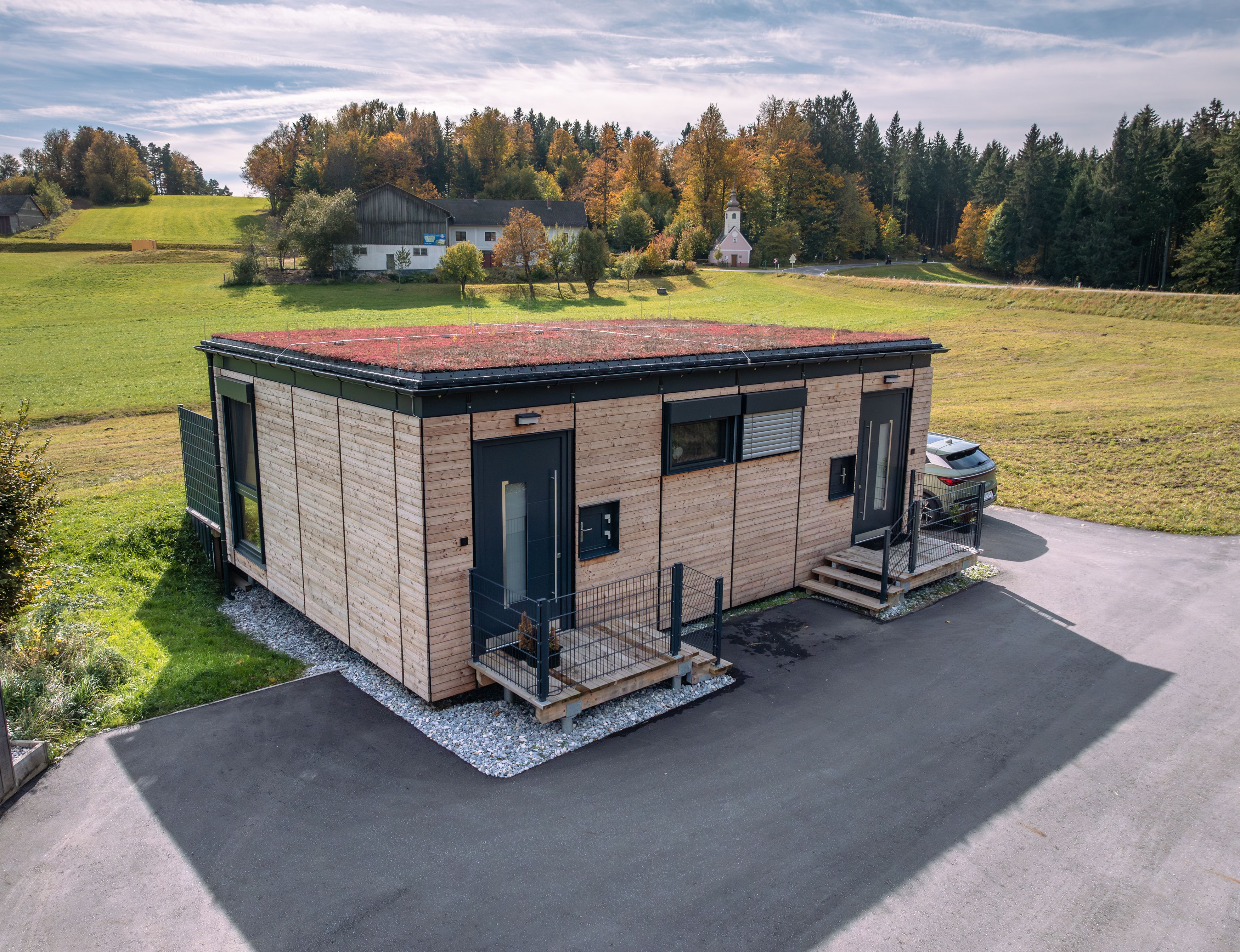 Modernes Holzhaus mit begrüntem Dach in ländlicher Umgebung.