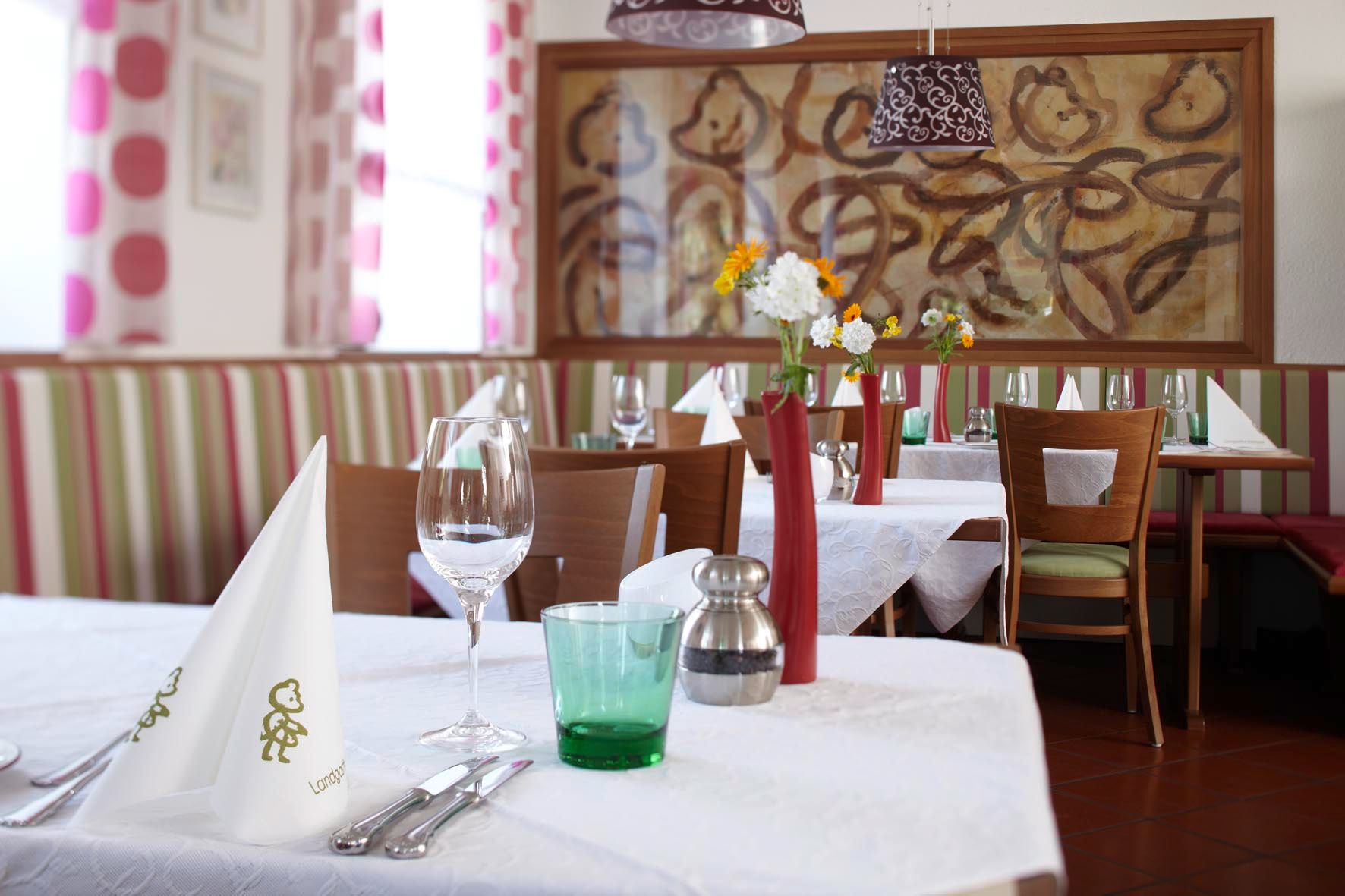 Innenansicht eines stilvoll gedeckten Restaurants mit weißen Tischdecken, Blumenvasen und Kunst an der Wand.