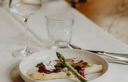 Ein kunstvoll angerichteter Teller präsentiert zarten Rehrücken, umgeben von frischem Spargel und verführerischen Lavendelkirschen. Die harmonische Komposition aus Farben und Aromen lädt dazu ein, die kulinarischen Köstlichkeiten der Region zu entdecken und zu genießen.