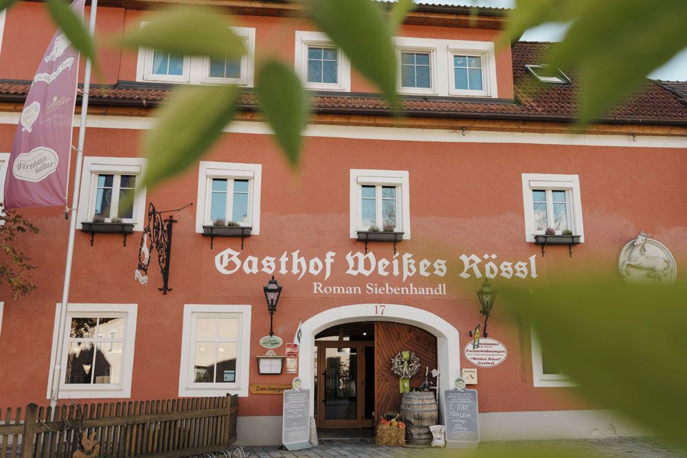 Fassade des Gasthofs Weißes Rössl in Mühldorf mit roter Wand und weißen Fenstern.