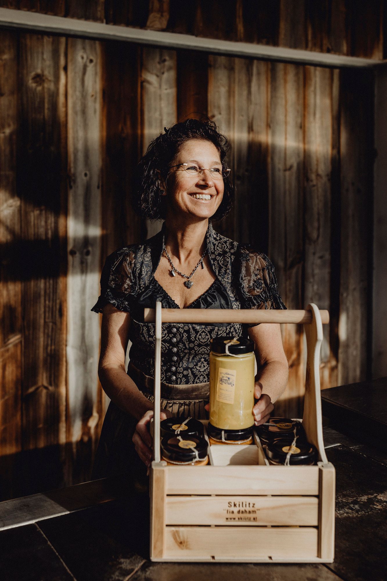 Frau in traditioneller Kleidung mit Holzkiste voller Gläser.