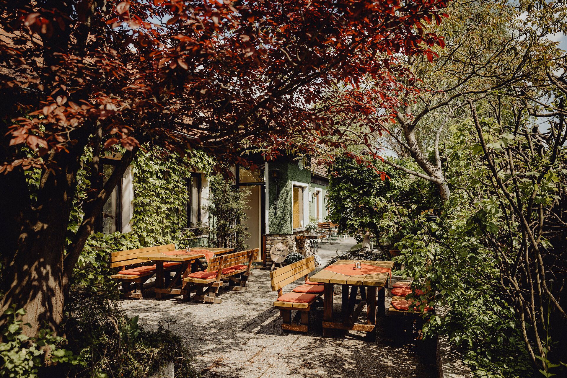 Umgeben von üppigem Grün und buntem Laub lädt die Terrasse zu entspannten Stunden im Freien ein. Die rustikalen Holztische und Bänke versprechen gesellige Zusammenkünfte, während die sanfte Brise die warmen Sommertage erfrischt.