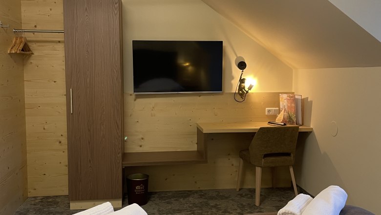 Gemütliches Doppelzimmer mit zwei Betten, einem Schreibtisch, einem Fernseher und einem Kleiderschrank.