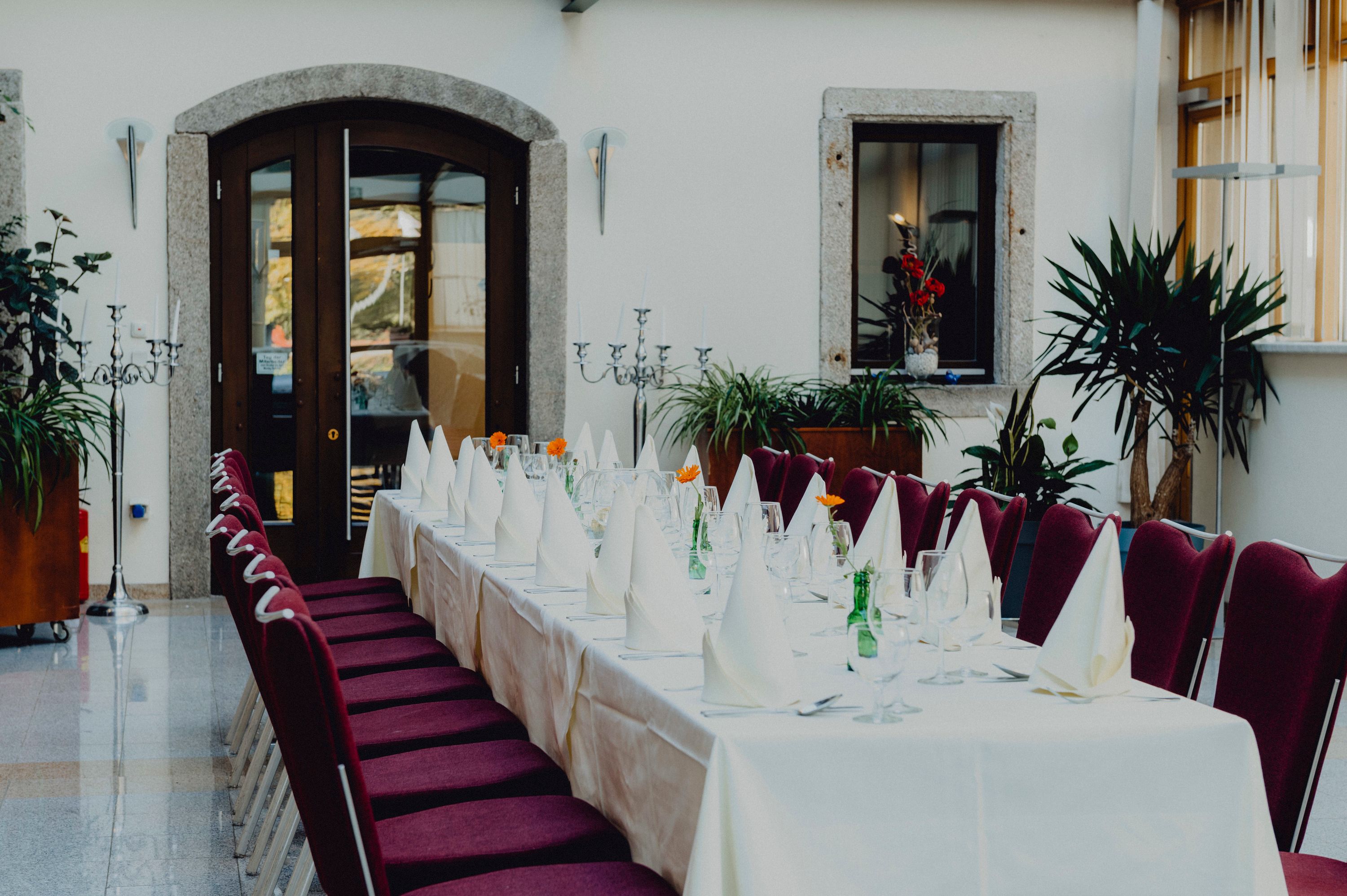 Elegant dining room with table setting, red chairs and plants.