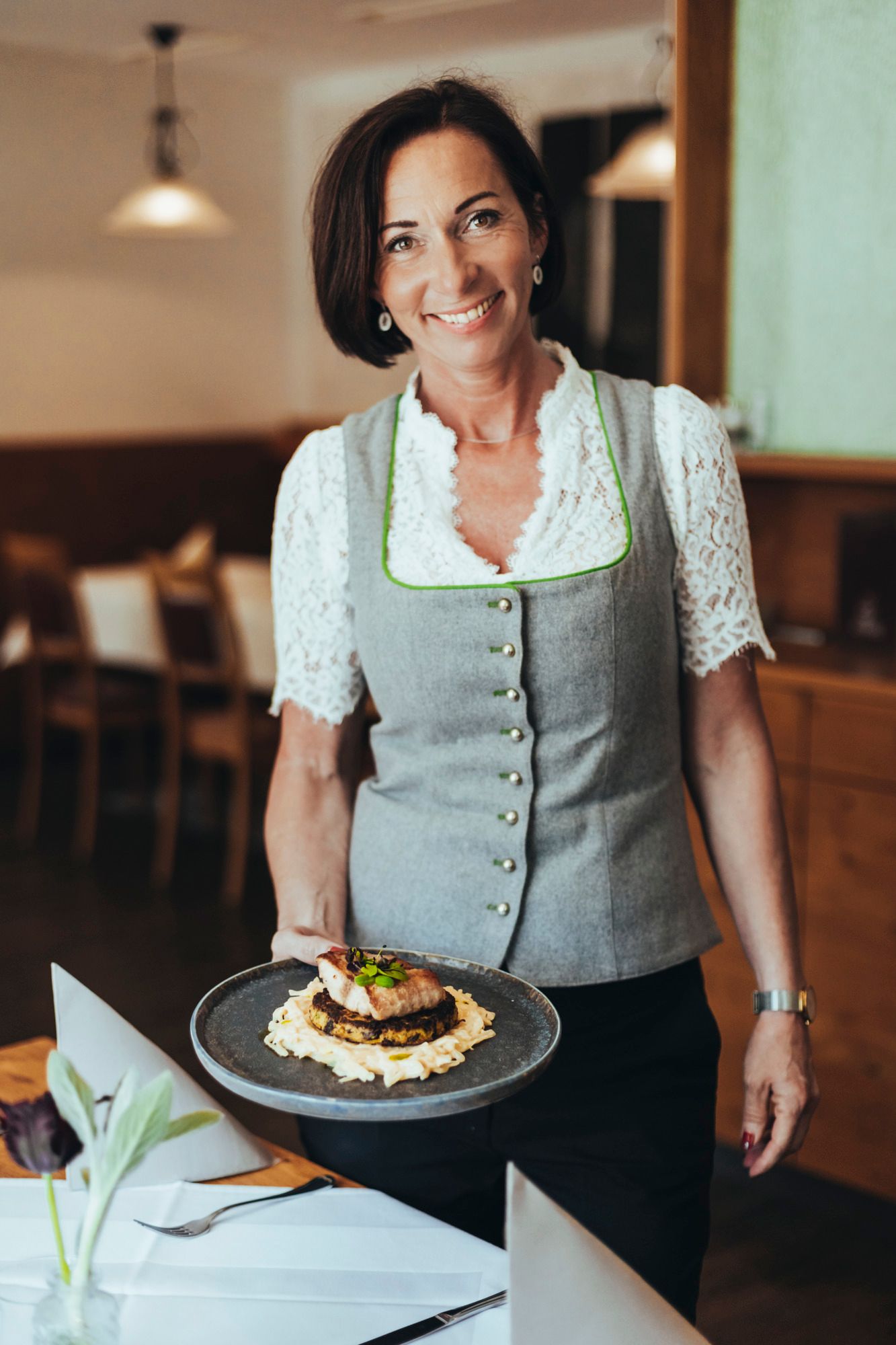 Frau in traditioneller Kleidung serviert ein Gericht auf einem Teller in einem Restaurant.