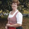 Frau in traditioneller Tracht vor einem Baum im Freien.