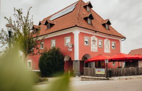 Ein rotes Geb&auml;ude mit roten Sonnenschirmen und Solarpanelen auf dem Dach.