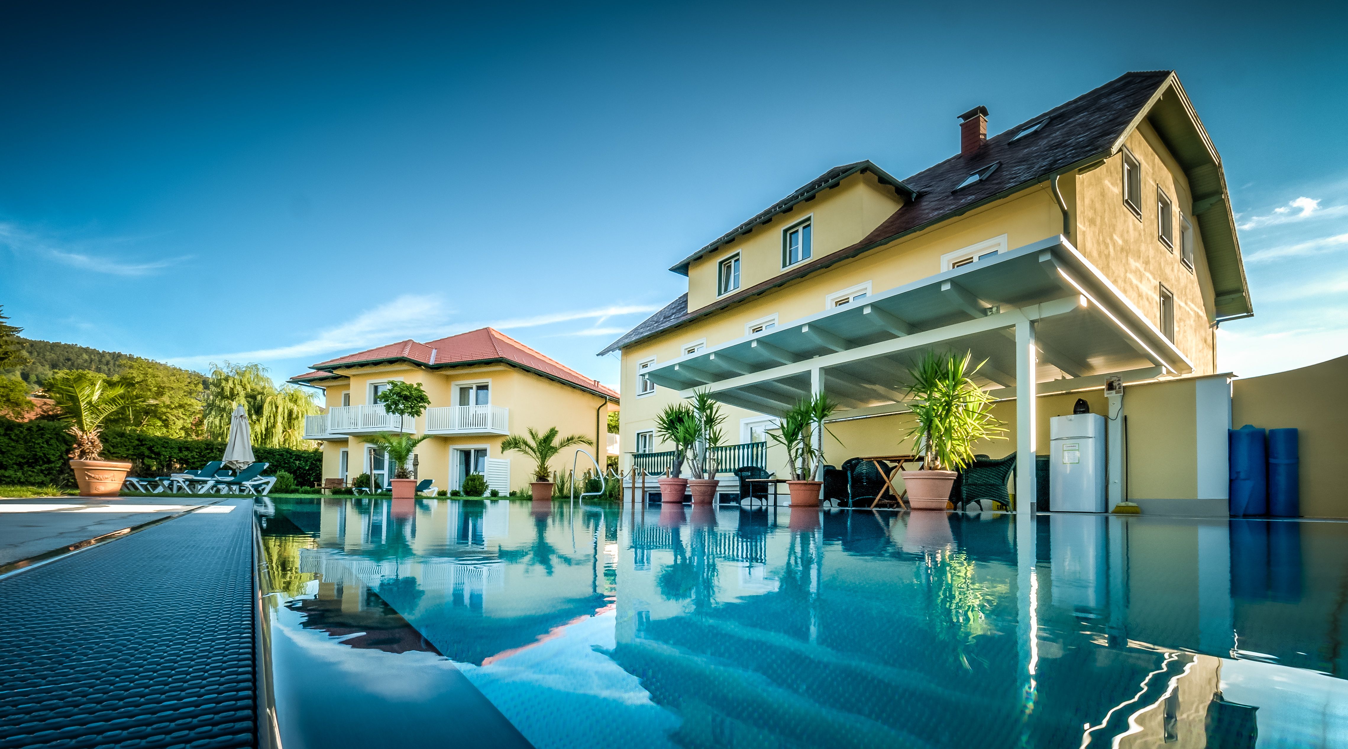 The garden villa with large pool in the foreground, surrounded by plants and sun loungers.