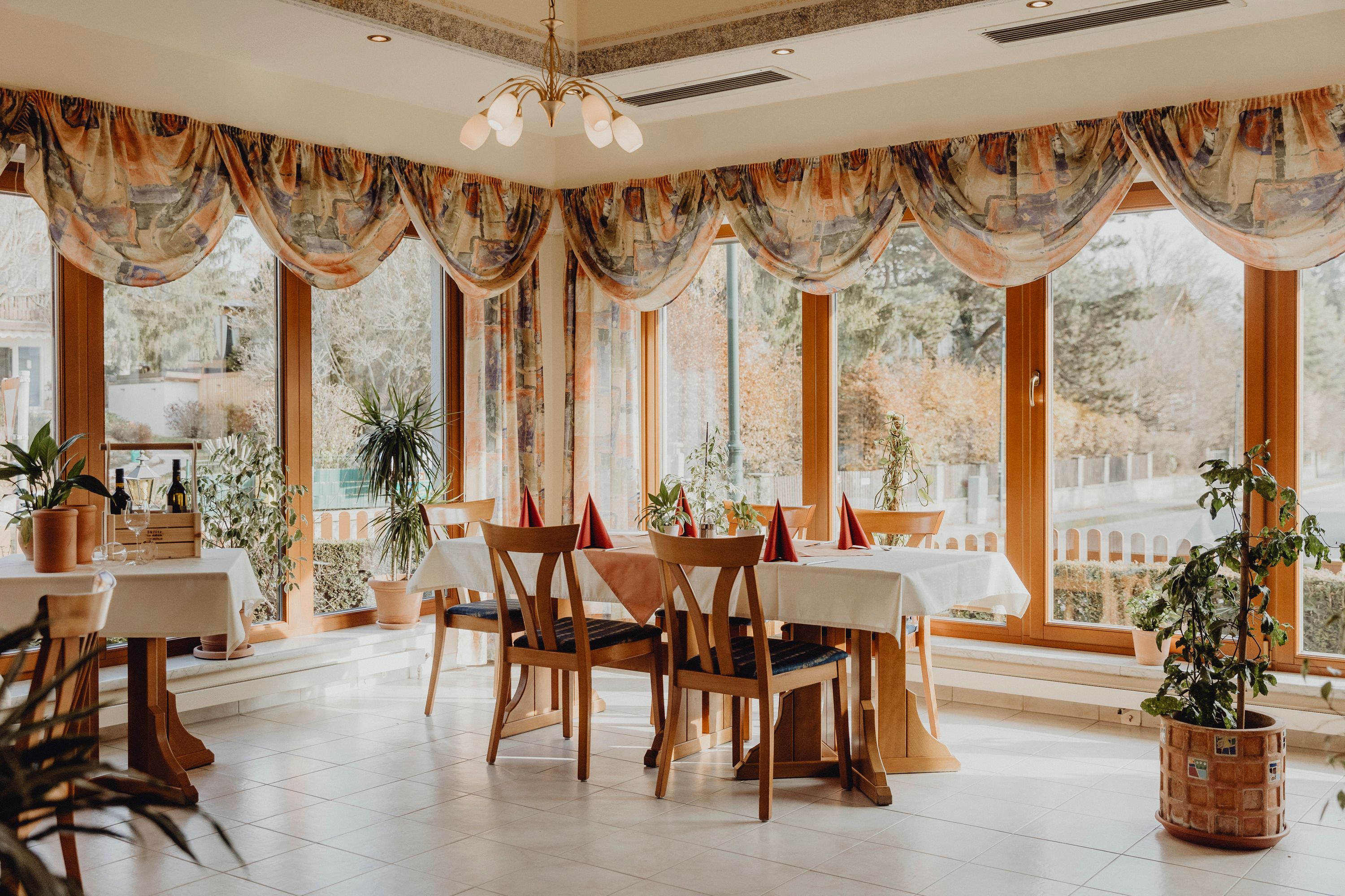 Ein helles Restaurant mit großen Fenstern, Holzmöbeln und Pflanzen.