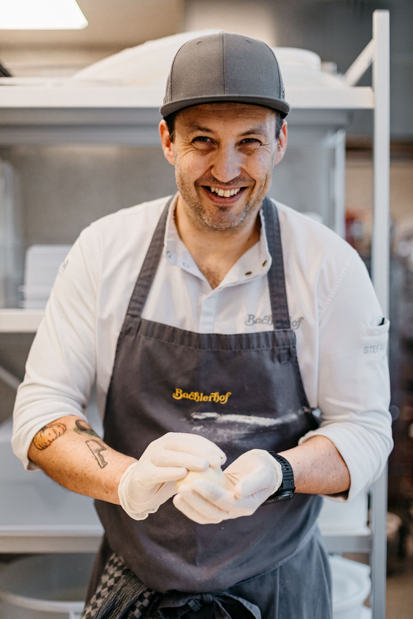 Ein lächelnder Koch mit Schürze und Handschuhen formt Teig in einer Küche.