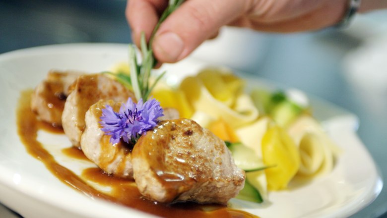 Ein Teller mit Fleisch, So&szlig;e, Nudeln und Gem&uuml;se, dekoriert mit einer Blume und Rosmarin.