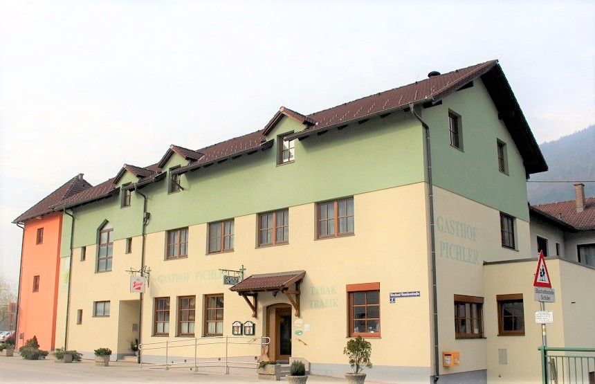 Ein zweistöckiges Gebäude mit der Aufschrift 'Gasthof Pichler', gelb und grün gestrichen, mit braunem Dach und mehreren Fenstern.