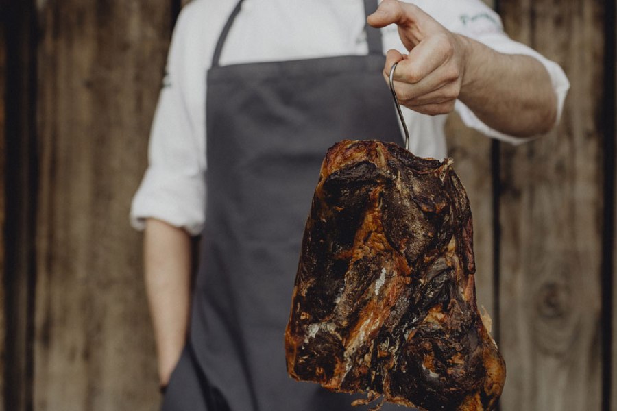 Person hält geräucherten Schinken an einem Haken.