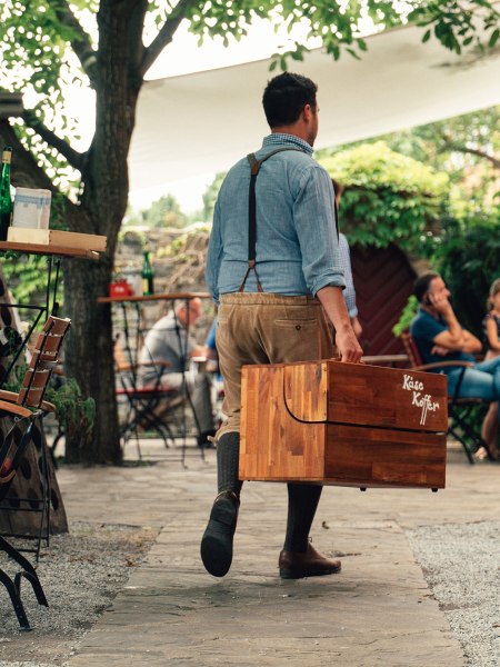 Der Maitre tr&auml;gt einen Holzkoffer mit der Aufschrift 'K&auml;sekoffer'