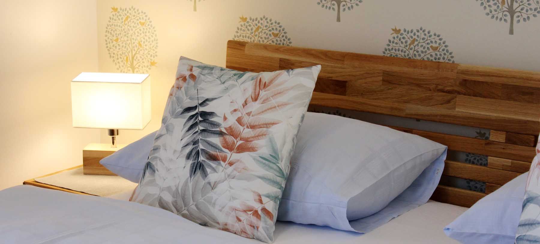 Nahaufnahme eines Bettes mit Holzkopfteil, dekorativen Kissen und Nachttischlampe.