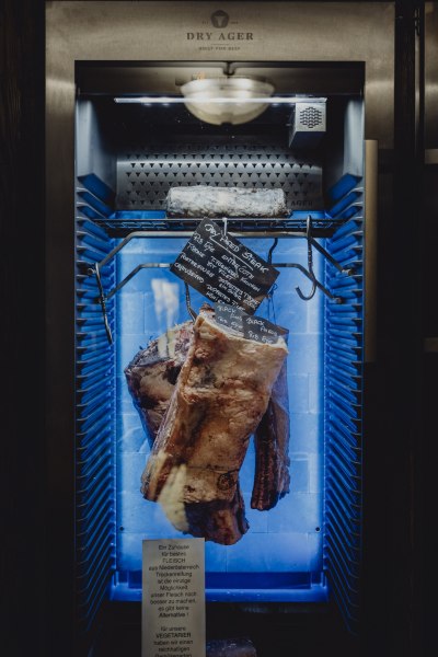 Ein Dry Ager K&uuml;hlschrank mit h&auml;ngendem Fleisch und einer Tafel mit Informationen.