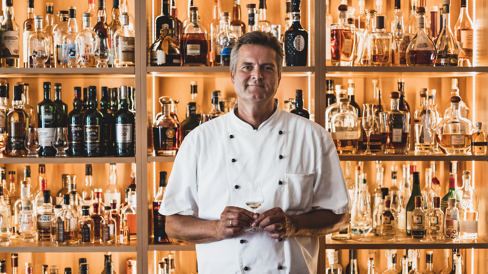 In einem einladenden Landgasthaus, umgeben von einer Vielzahl erlesener Getränke, strahlt der Wirt mit einem Glas in der Hand Gastfreundschaft und Leidenschaft für die Kulinarik aus. Die warme Atmosphäre und die sorgfältig ausgewählten Spirituosen laden dazu ein, die regionalen Köstlichkeiten zu genießen und unvergessliche Momente zu erleben.