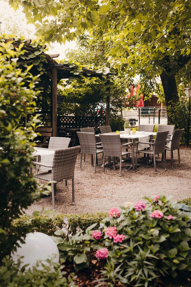 A cozy garden area with tables and chairs under trees, surrounded by plants and flowers.