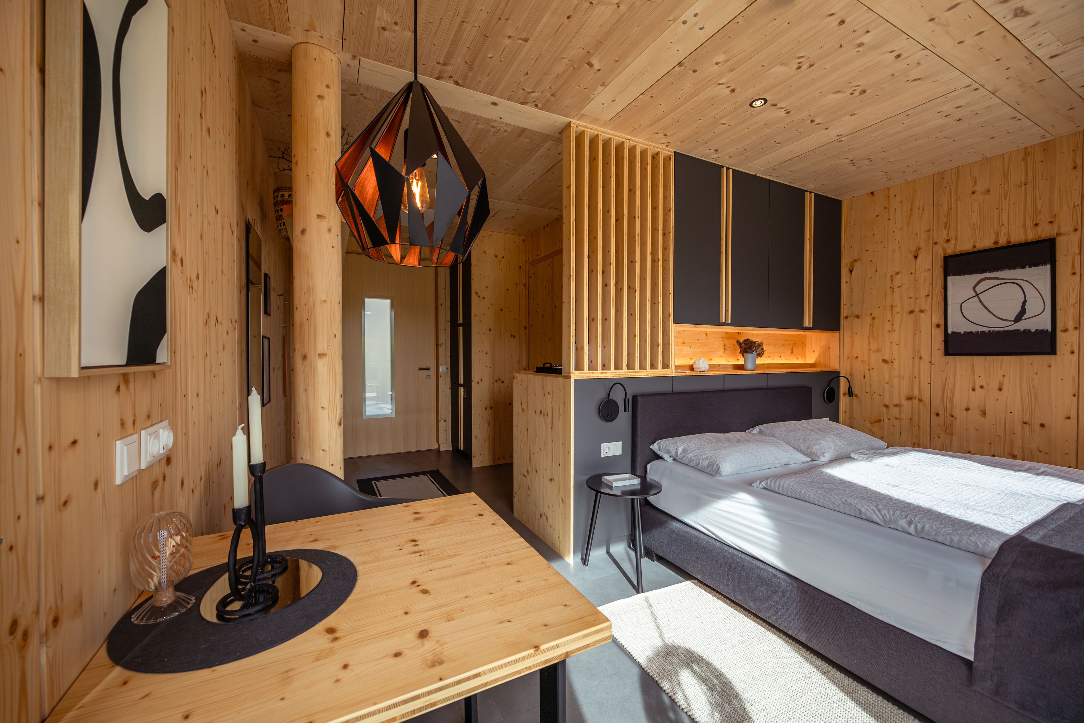 Modernes Schlafzimmer mit Holzwänden, einem Bett, einem Tisch und einer geometrischen Hängelampe.