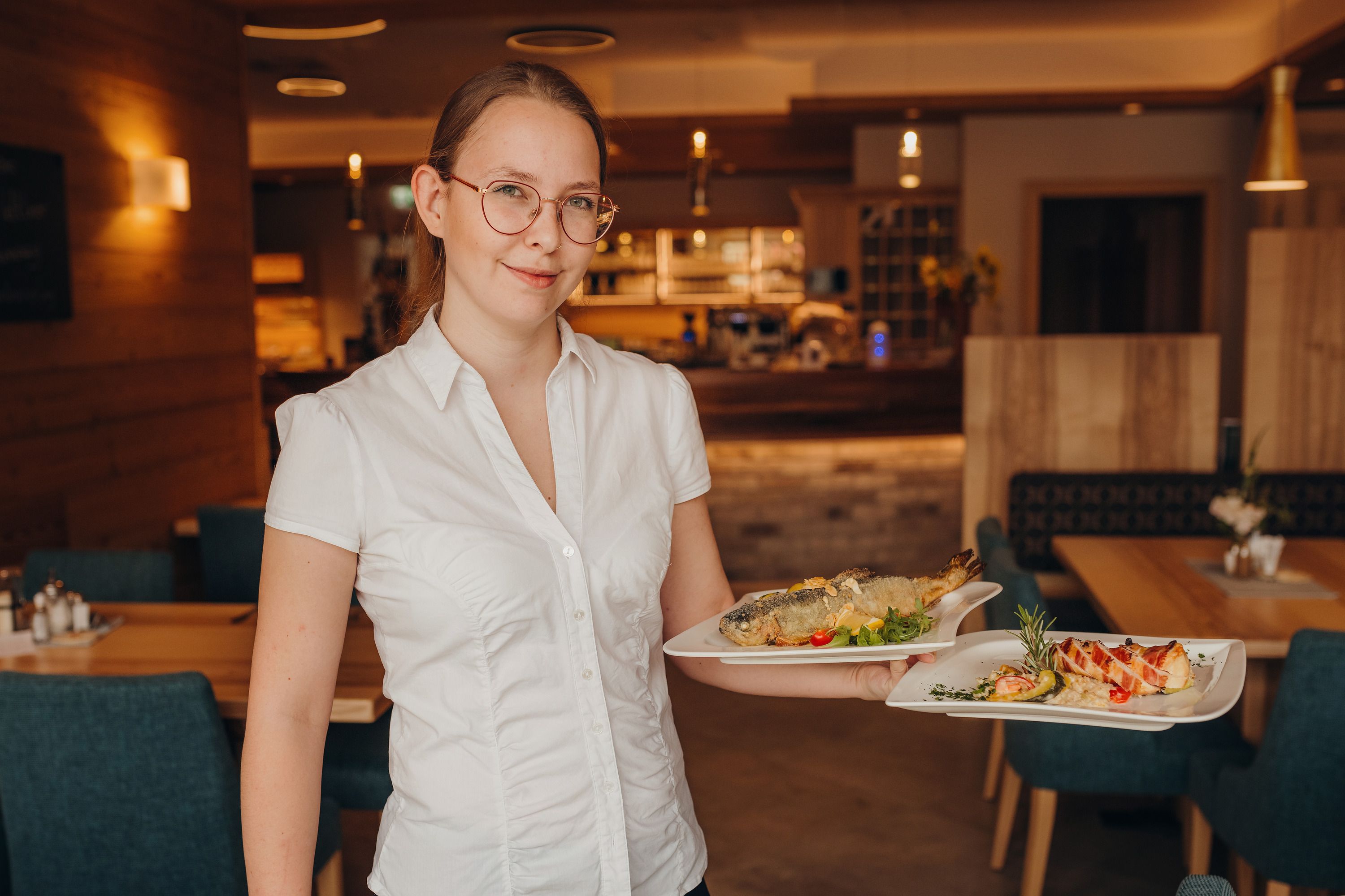 Eine Frau in einem Restaurant trägt zwei Teller mit Speisen.