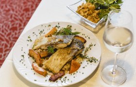 Gourmetgericht mit Fischfilet, Gemüse und Weißwein auf weißem Tisch.