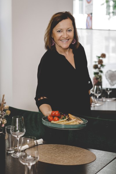 Eine Frau in schwarzer Kleidung serviert ein Gericht mit Tomaten und Fisch in einem Restaurant.