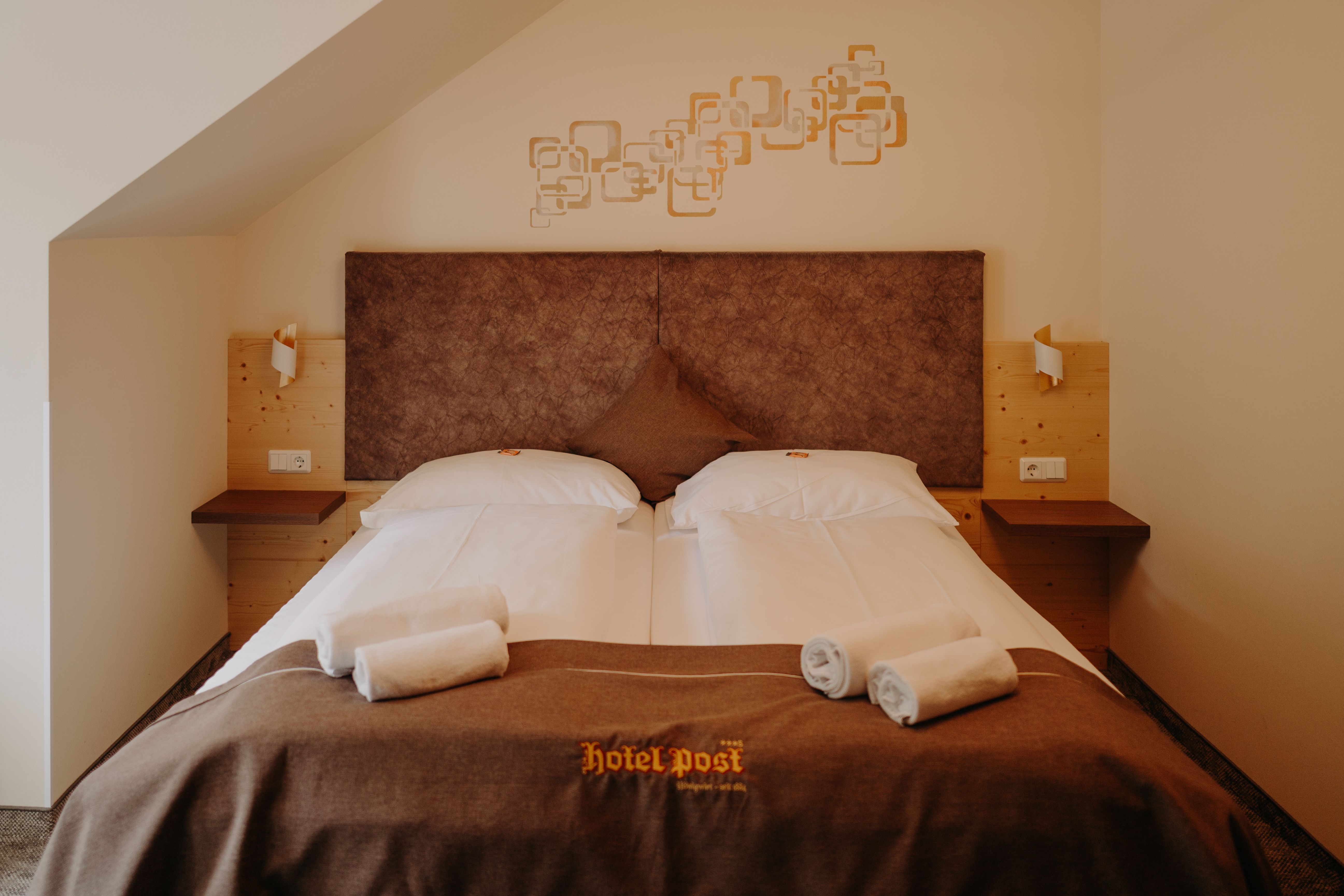 Gemütliches Hotelzimmer mit Doppelbett, mit heller Holzverkleidung und erdigen Farbtönen.