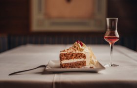 Ein St&uuml;ck Torte mit Sahne und ein Glas Lik&ouml;r auf einem gedeckten Tisch.