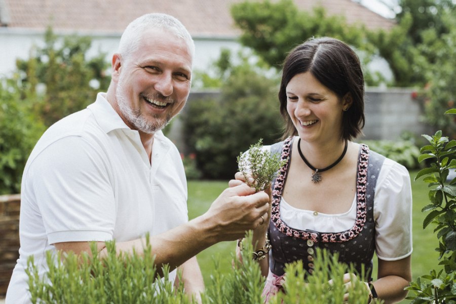 Ein Mann und eine Frau stehen l&auml;chelnd in einem Garten und betrachten Kr&auml;uter.