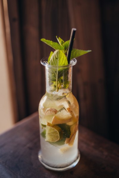 Ein Glas mit einem erfrischenden Getränk, Eiswürfeln, Limettenscheiben und Minzblättern, auf einem Holztisch.