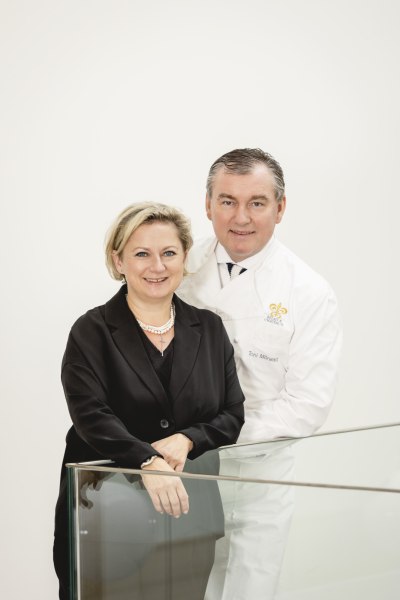 Ein Mann und eine Frau posieren lächelnd vor einem weißen Hintergrund.