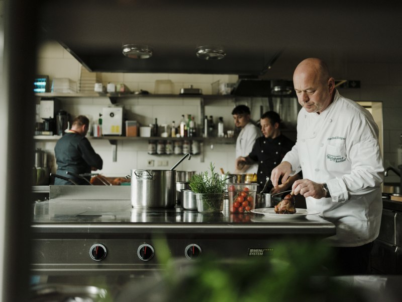 Köche arbeiten in einer professionellen Küche, einer schneidet Fleisch.