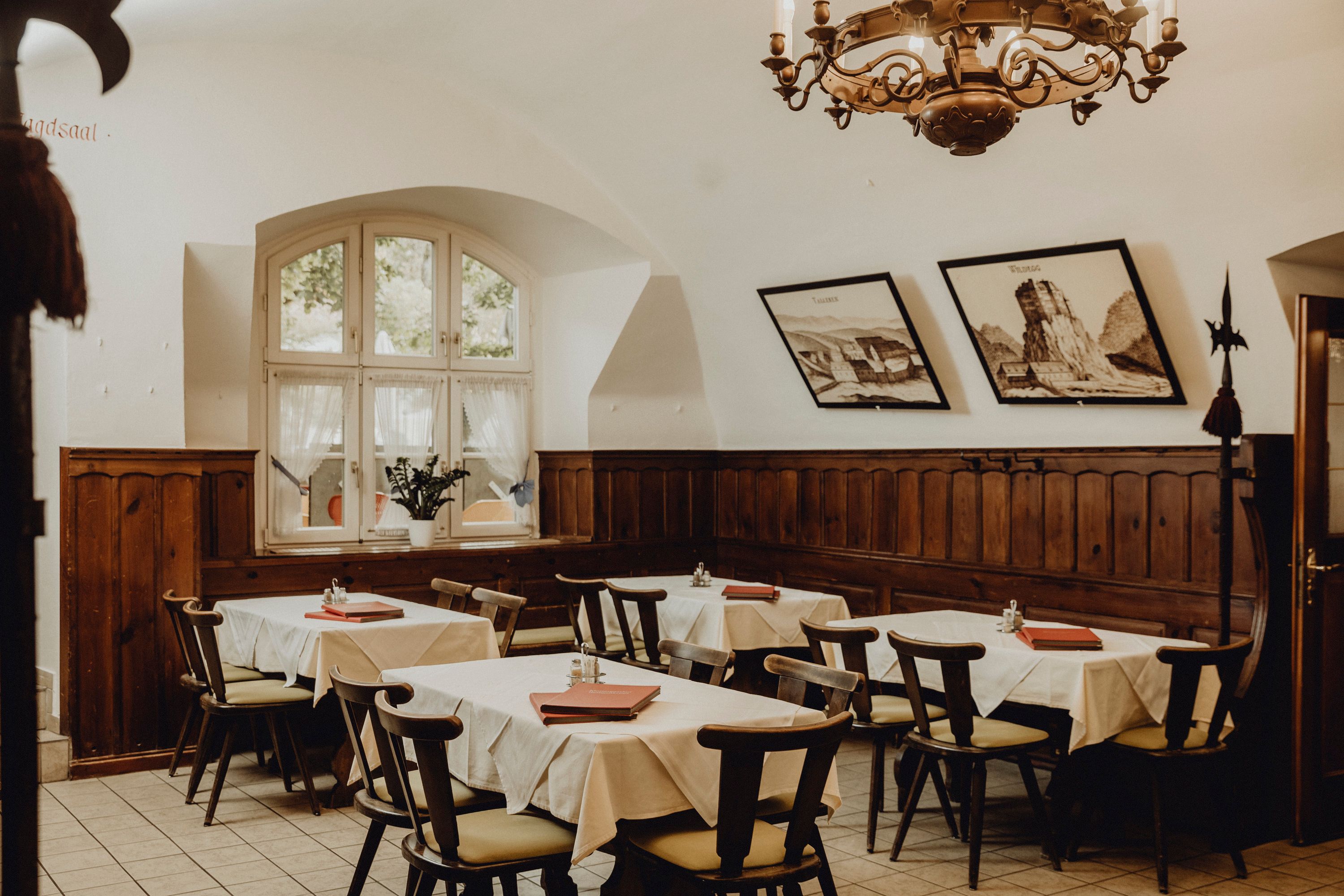 Gemütlicher Gastraum mit Holzmöbeln, weißen Tischdecken und Wandbildern.