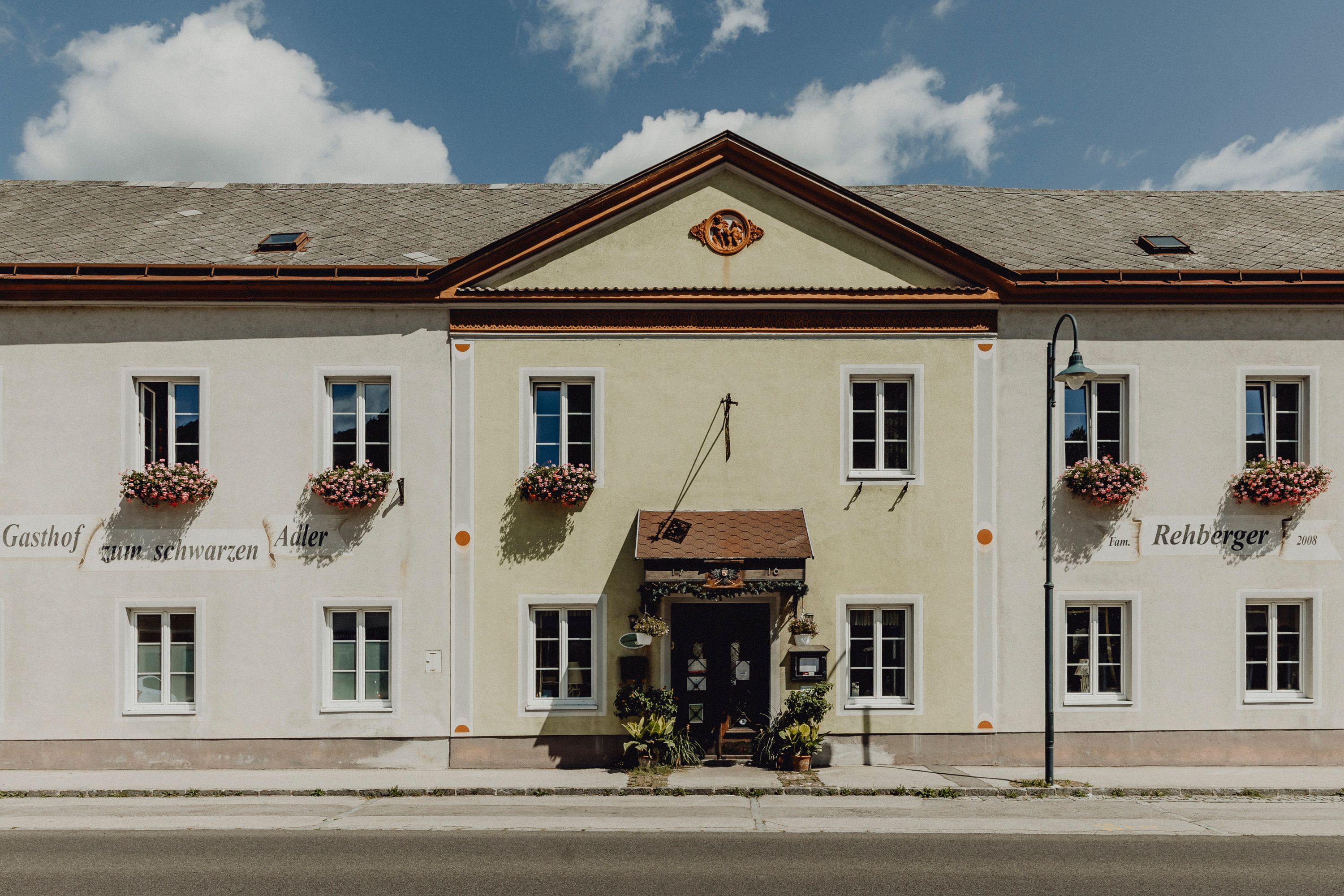 Facade of an inn with flowers on the windows and a sign with the inscription 'Gasthof zum schwarzen Adler'.