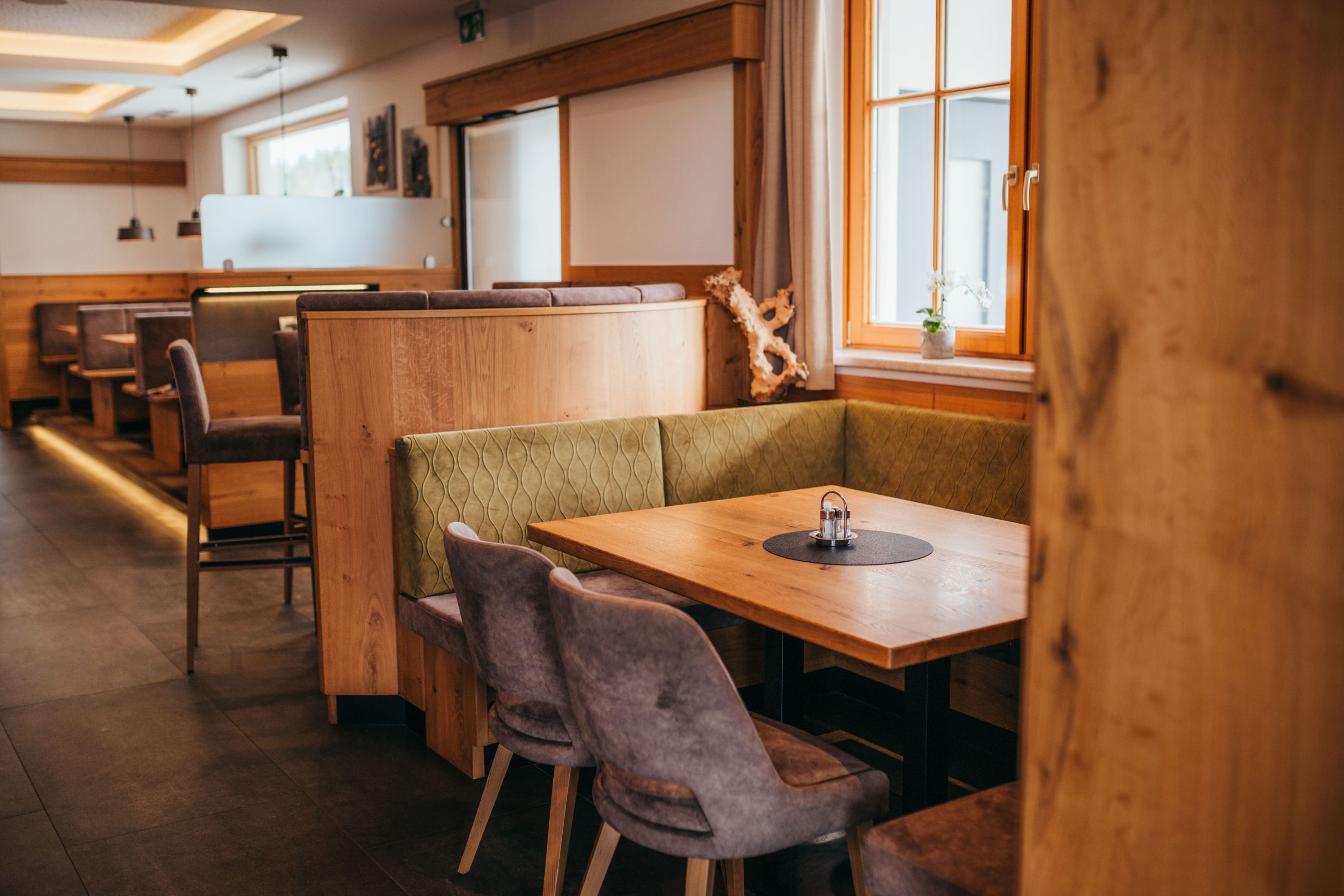 Gemütliche Gaststube mit Holzmöbeln und gepolsterten Sitzbänken, Fenster mit Vorhängen, Tisch mit Salz- und Pfefferstreuer.