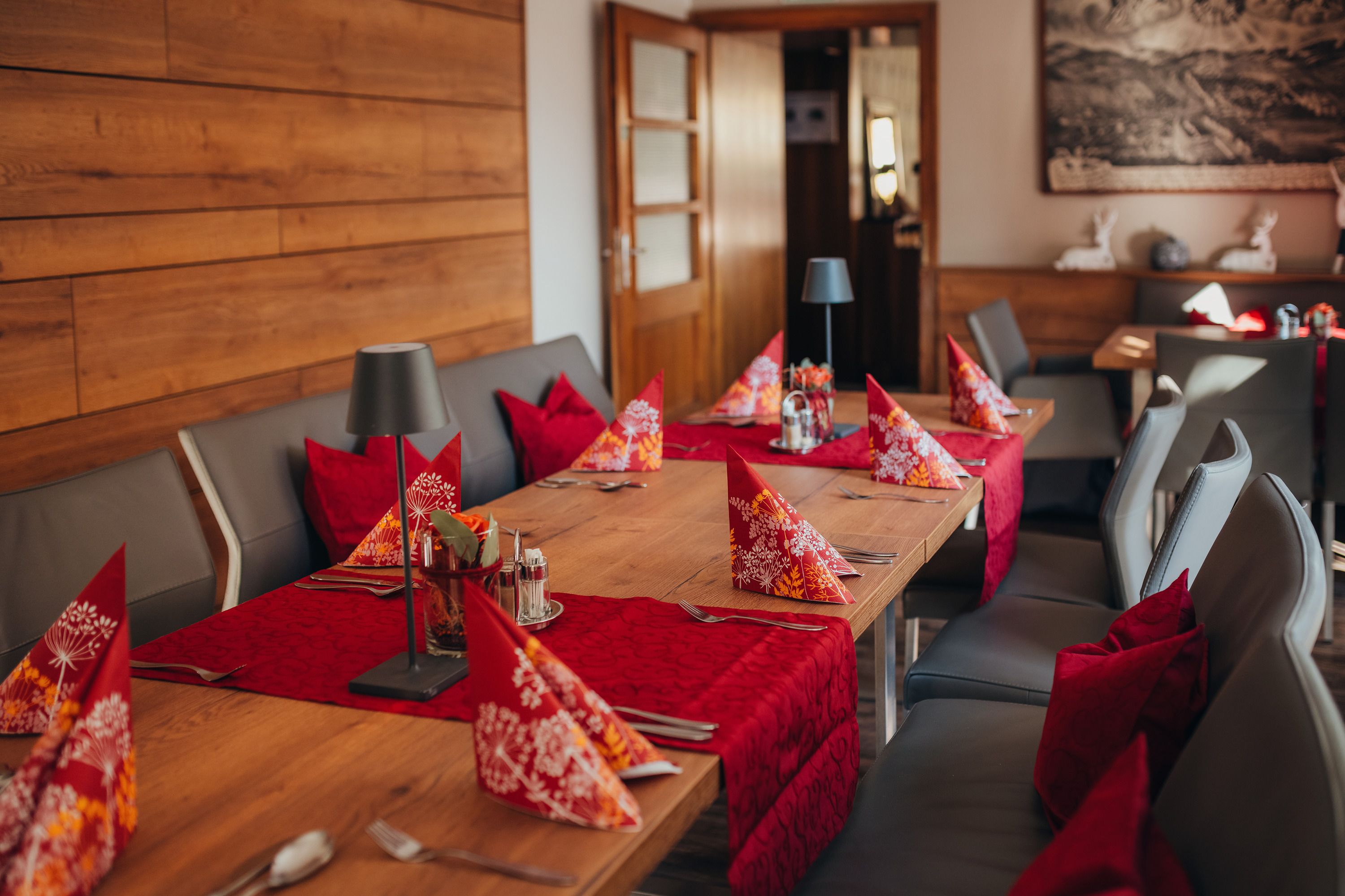 Gemütlich gedeckter Tisch in einem Restaurant mit roten Servietten und Tischläufern.